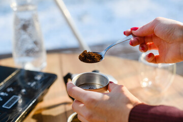 A female hand with spoon of ground coffee is filled with a geyser coffee maker.