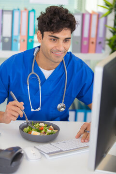young male doctor having lunch at office using computer