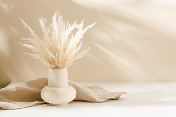Ceramic vase with natural pampas grass and beige linen towel at the background with warm shadows,...