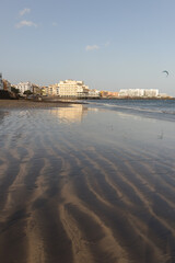 Seascape of yellow sand beach and picturesque village in the background. Playa Grande, El Medano, Tenerife, Canary Islands. Spain