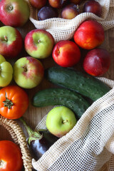 Straw bag and reusable fabric bags filled with various healthy fruit and vegetables. Wooden background, top view.