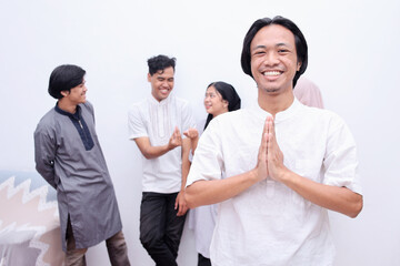 Muslim man showing greeting gesture and smiling to camera against friends as the background