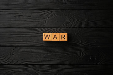 Wooden cubes with the word War on a black wooden table. Word is made of letters from yellow wood on a dark background. Flat lay, top view, black backdrop.