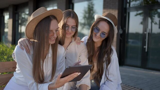 Three young beautiful woman girl hipster friends in summer relaxing using digital tablet looking at photo laughing surfing Internet street outdoor. Friendship having fun. happiness freedom love 