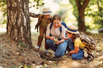 Happy mother and two   children in   with backpacks examining environment through magnifying glass...