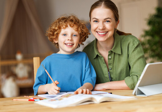 Cheerful mother doing homework with son at home