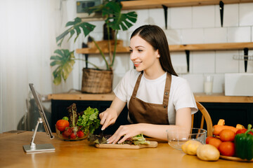 Young American woman learning online cooking class via tablet computer in kitchen