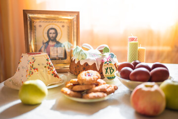 Easter cake with painted eggs, apples and cookies on table in home kitchen. Church icons and candle on background. Orthodox religion theme.