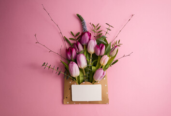 Pink and purple tulips in a paper envelope on a pink background copy space
