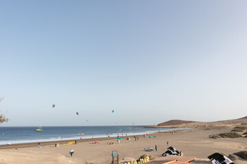 Fototapeta na wymiar seascape, views of the yellow sand beach, bushes, people practicing kite surfing and Montaña Roja in the background. Paya Grande, El Medano, Tenerife, Canary Islands. Spain