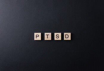 The letters PTSD on wooden blocks on a black background. Minimal concept post traumatic stress disorder.