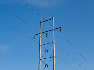 Three power lines suspended on a cross member between two wooden poles. Power insulators are...