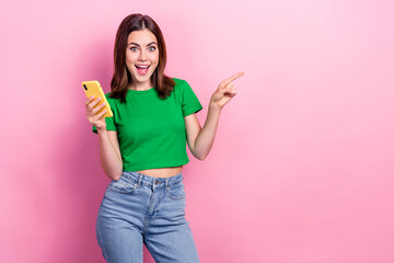 Portrait of astonished charming blogger girl hold smart phone direct finger empty space promo isolated on pink color background