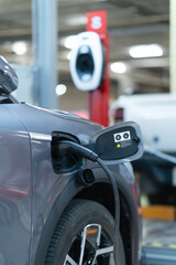 Fototapeta premium Power cable pump plug in charging power to electric vehicle EV car with modern technology UI control information display, car fueling station connected power cable alternative sustainable eco energy