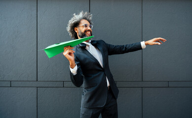 Cinematic and storytelling image of a young entrepreneur throwing a green paper aircraft in the...