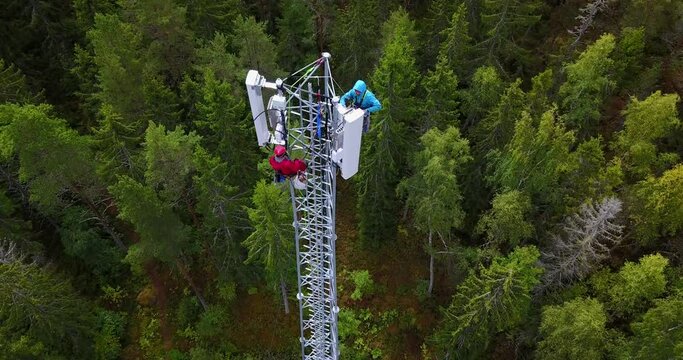 Drone point of view of a telecommunications technicians working at height on a telecom tower, performing maintenance on 5G antenna. 