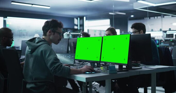 Group of Diverse Multicultural Men and Women Working on Desktop Computers in a Research Center. Young Software Developer Working on a Computer with Two Green Screen Mock Up Displays