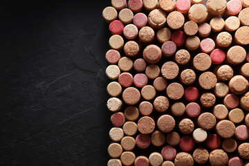 Many wine bottle corks on black table, flat lay. Space for text