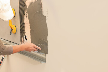 Worker spreading adhesive mix on wall for tile installation indoors, closeup