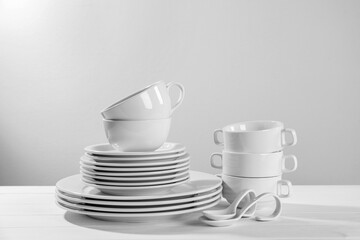 Set of clean dishware on white wooden table against light background