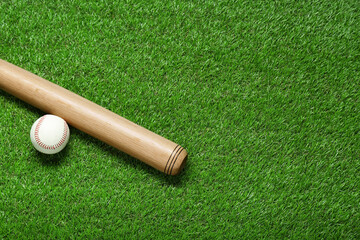 Wooden baseball bat and ball on green grass, flat lay. Space for text