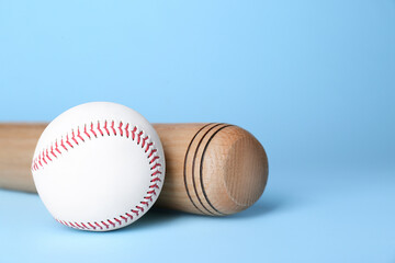 Wooden baseball bat and ball on light blue background, space for text. Sports equipment