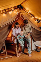 Obraz na płótnie Canvas Happy family with lovely baby relaxing and spend time together in glamping on summer evening. Luxury camping tent for outdoor recreation and recreation. Lifestyle concept