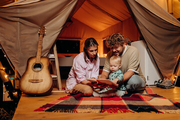 Happy family with lovely baby playing and spend time together in glamping on summer evening. Luxury camping tent for outdoor recreation and recreation. Lifestyle concept