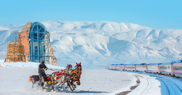 Red diesel train (East express) in motion at the snow covered railway - Horses pulling sleigh in winter - Ani Ruins, Ani is a ruined and  medieval Armenian city - Kars, Turkey