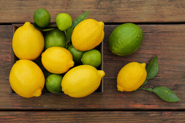 Many fresh lemons and limes with leaves on wooden table, flat lay