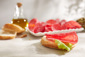 slice of salami with bread and olive oil. sandwich with sausage and herbs. snack on a light table. meat delicacy under sunlight. antipasto close up. 