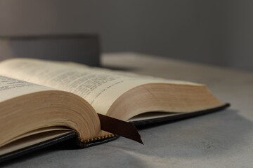 Closeup view of open hardcover Bible on grey table indoors, space for text. Religious book
