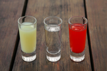 Shots with lime juice, tequila and sangria as colors of mexican flag on wooden table, closeup. Traditional serving