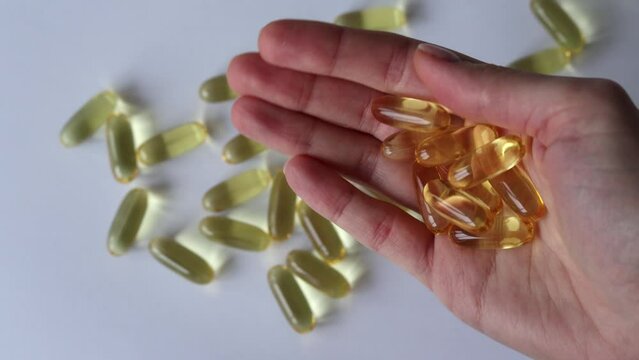 Fish oil in a woman's hand on a white background with scattered capsules.