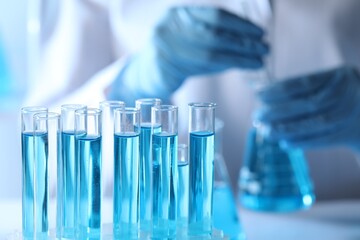 Scientist holding flask near test tubes with light blue liquid, selective focus
