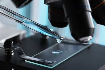 Dropping light blue liquid from pipette on glass slide in laboratory, closeup