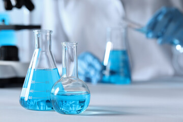 Closeup view of scientist pouring light blue liquid from test tube into flask and laboratory glassware on table, selective focus