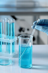 Scientist taking sample of light blue liquid in laboratory, closeup