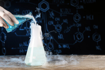 Scientist working with laboratory glassware and space for text at wooden table, closeup. Chemical...