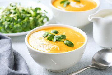 Butternut squash cream soup garnished with heavy cream and fresh sunflower microgreen. Creamy pumpkin fall soup in white bowl on the gray table. Selective focus