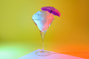 Beautiful martini glass with cotton candy and umbrella on color background