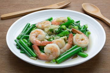 close up of stir fried shrimp with onion flower stem in a ceramic dish on wooden table. asian homemade style food concept.