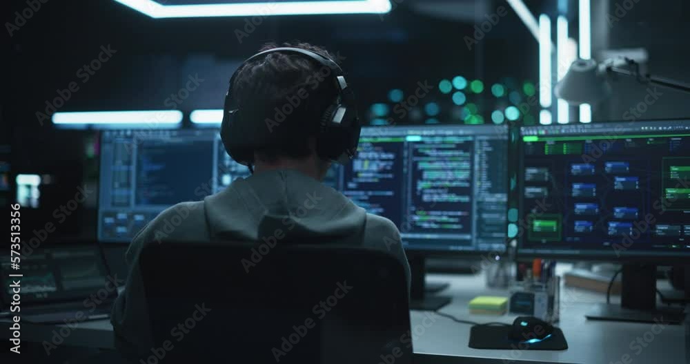 Poster System Administrator Working in a Dark Research Facility on a Computer with Multiple Displays. Software Developer in Casual Clothes Wearing Headphones and Updating Server System Database