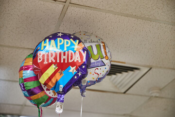 3 helium party balloons saying happy birthday beneath a shabby office cealing