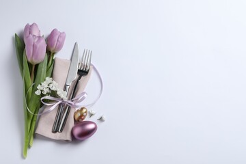 Cutlery set, Easter eggs and beautiful flowers on white background, flat lay with space for text. Festive table setting