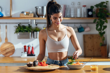 Fintess woman making a healthy poke bowl in the kitchen at home.