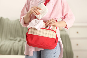 Woman putting diaper into mother`s bag indoors, closeup