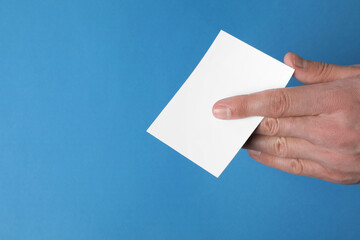 Man holding paper card on blue background, closeup. Mockup for design