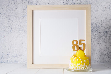 The number Eighty five on the yellow cake next to the white frame mockup with copy space.