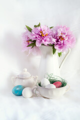 Easter still life with gorgeous pink peonies in a vase and an antique porcelain bowl with coloured eggs on a white background